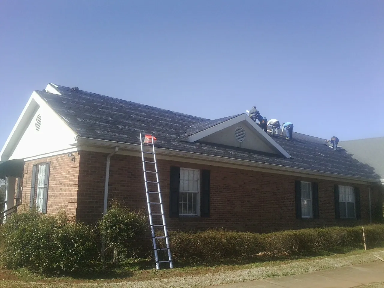 Crew tearing shingles off a brick ranch roof with a ladder set — Emergency Roof Repair work by our crew in North Bergen
