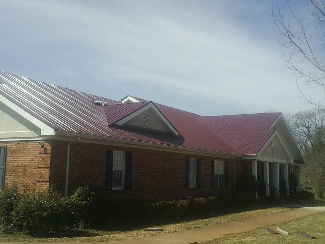 Red metal roof with gabled entries on a long brick building, from a Hail Damage Roof Repair job in North Bergen