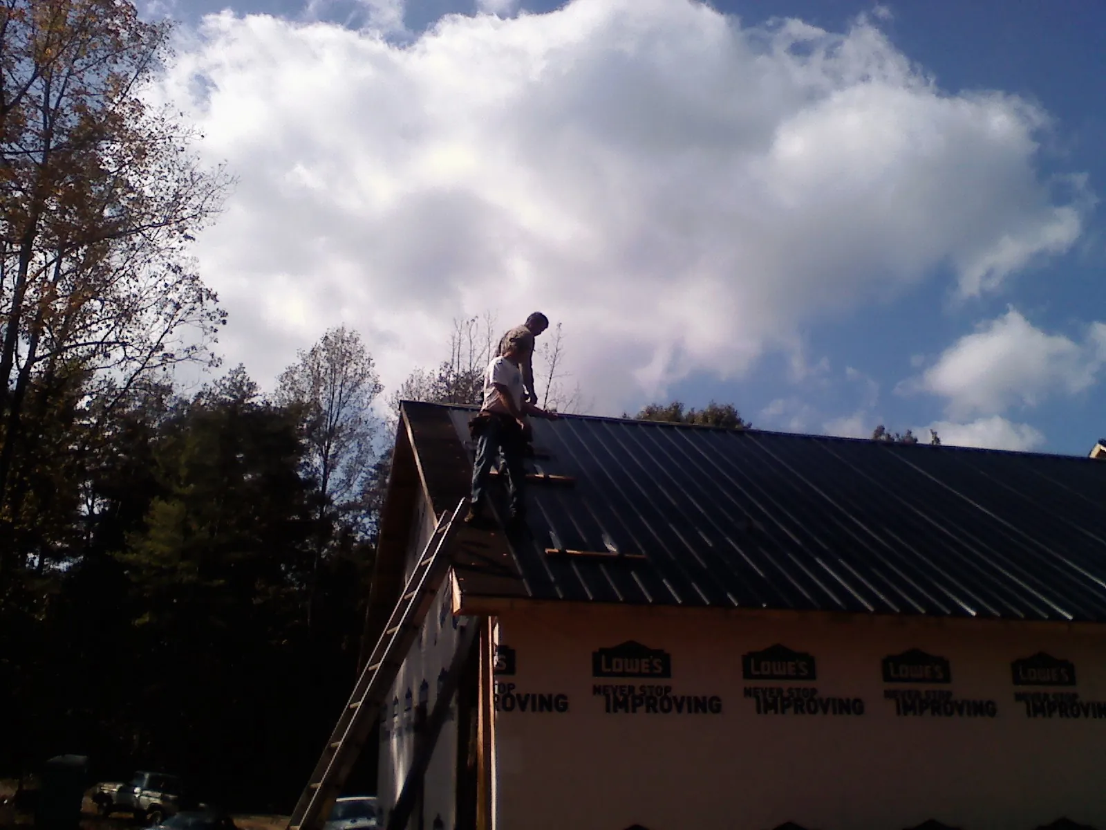 Roofer fastening dark metal panels high against a cloudy sky, from a Roof Inspection job in North Bergen