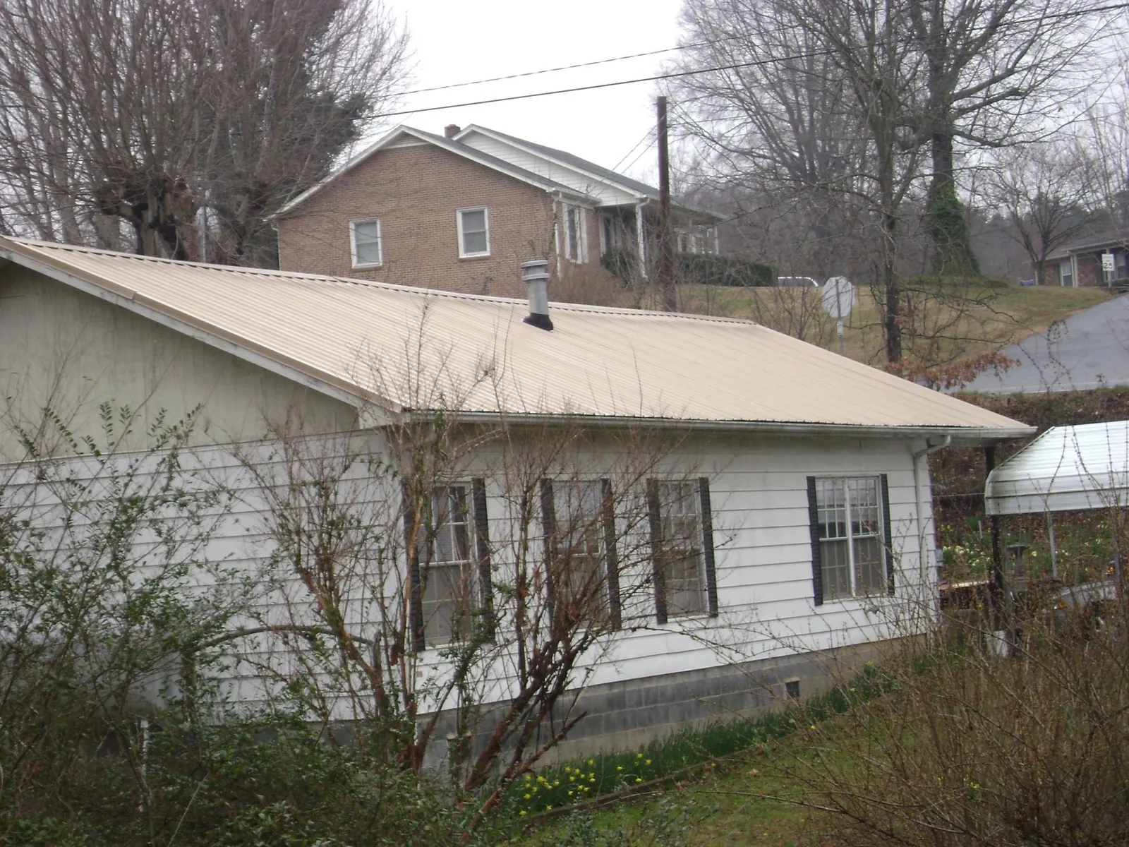 Tan metal roof on a white sided house set into a hillside — Commercial Roofing by Roofing Brothers in North Bergen
